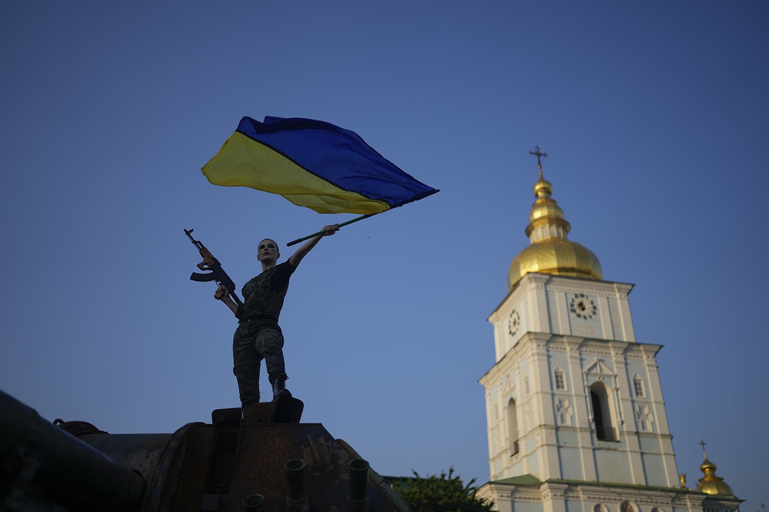  A woman brandishes a Ukrainian flag on top of a destroyed Russian tank in Kyiv, Ukraine, Friday, June 10, 2022. (AP Photo/Natacha Pisarenko) 