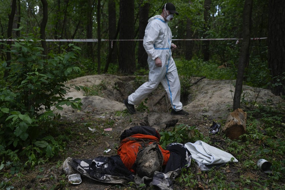  EDS NOTE: GRAPHIC CONTENT - A member of an extraction crew walks near a body found in the woods during an exhumation of a mass grave near Bucha, on the outskirts of Kyiv, Ukraine, Monday, June 13, 2022. (AP Photo/Natacha Pisarenko) 
