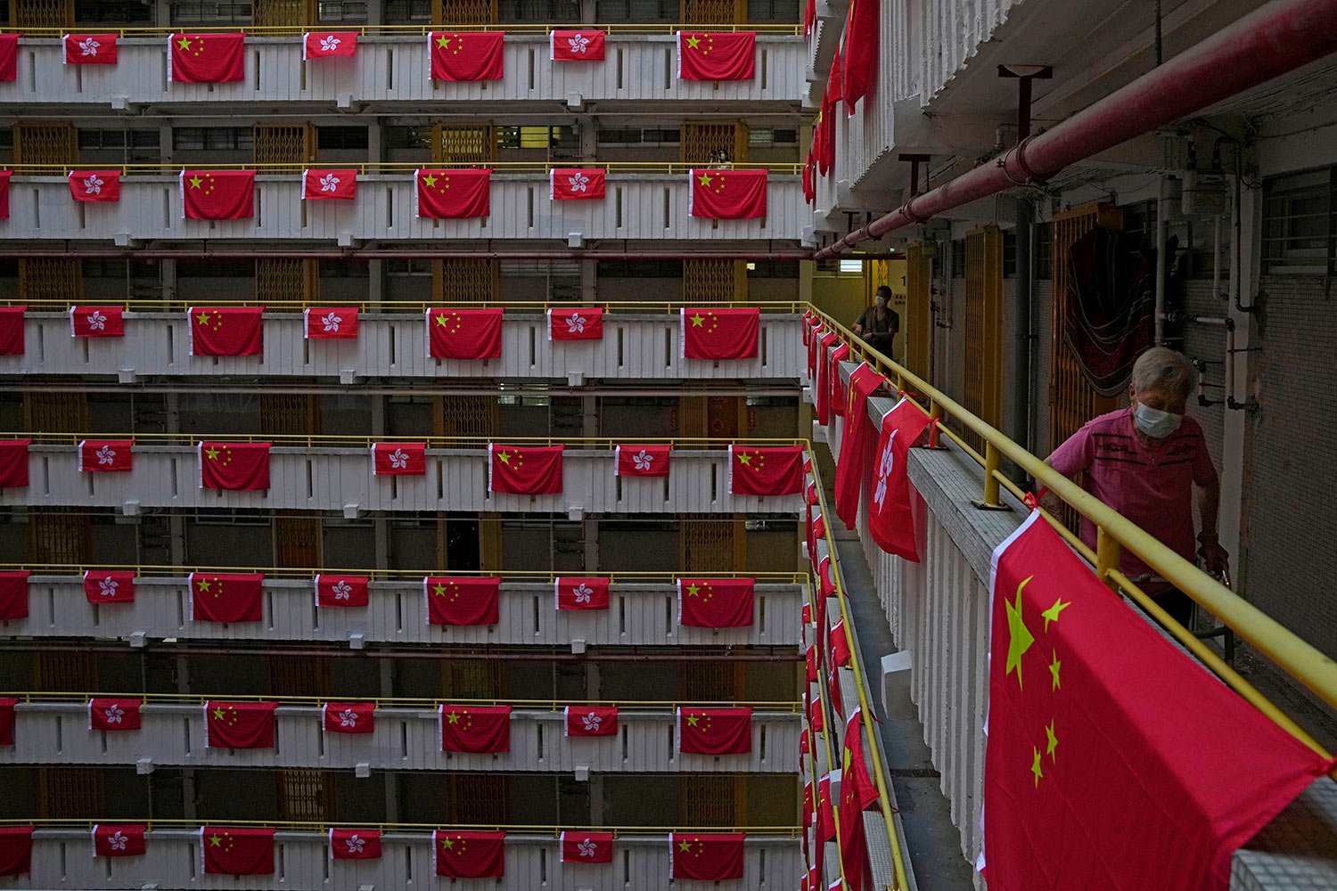  A resident walks besides the Chinese and Hong Kong flags hanging from a residential building to celebrate the 25th anniversary of Hong Kong handover to China, at a public housing estate, in Hong Kong, Saturday, June 25, 2022. (AP Photo/Kin Cheung) 