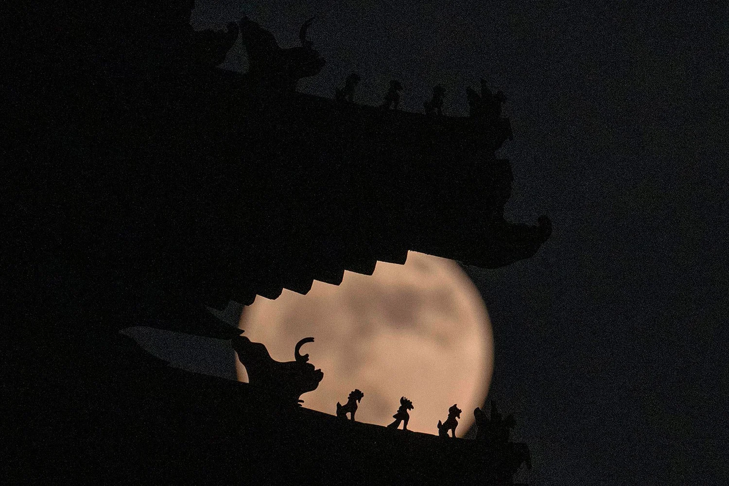 Roof decorations on the corner tower at the Forbidden City depicting sacred beasts are silhouetted against a supermoon, Tuesday, June 14, 2022, in Beijing. (AP Photo/Ng Han Guan)