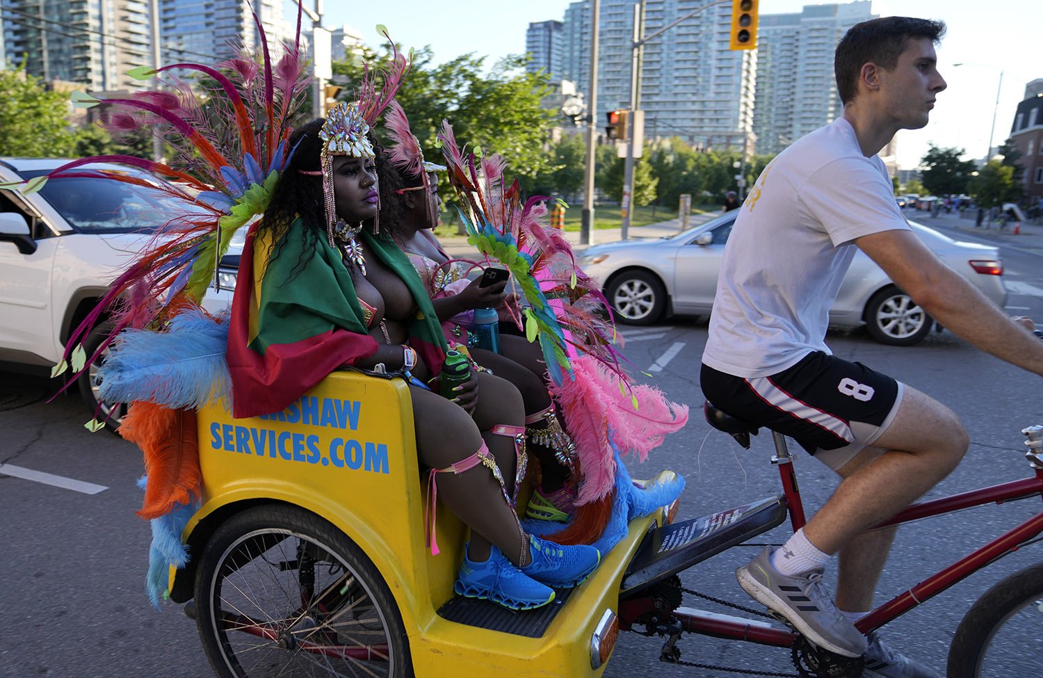  A rickshaw worker pedals costumed clients after they attended the Caribbean Carnival parade in Toronto, Canada, Saturday, July 30, 2022. (AP Photo/Kamran Jebreili) 