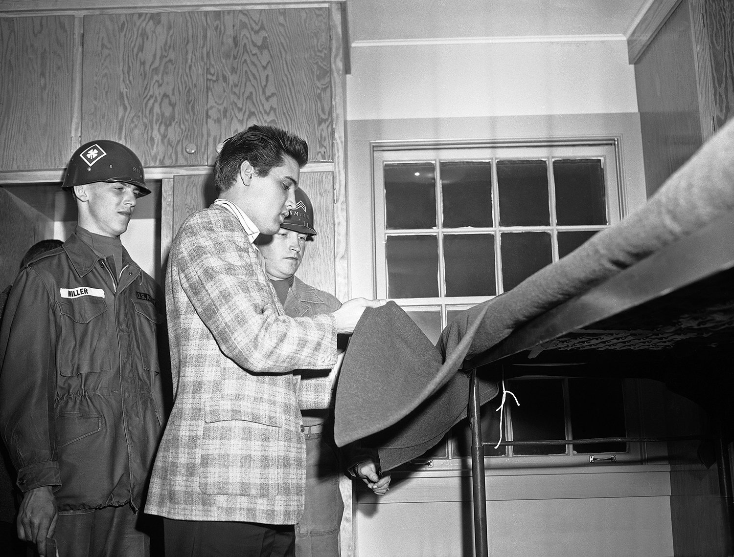 Under the watchful gaze of an instructor, Corporal John D. Smith, rock 'n' roll singer Elvis Presley adjusts a blanket on an upper bunk in Fort Chaffee, Ark. on March 25, 1958. Presley and 21 other recruits arrived from the Memphis, Tenn. induction 