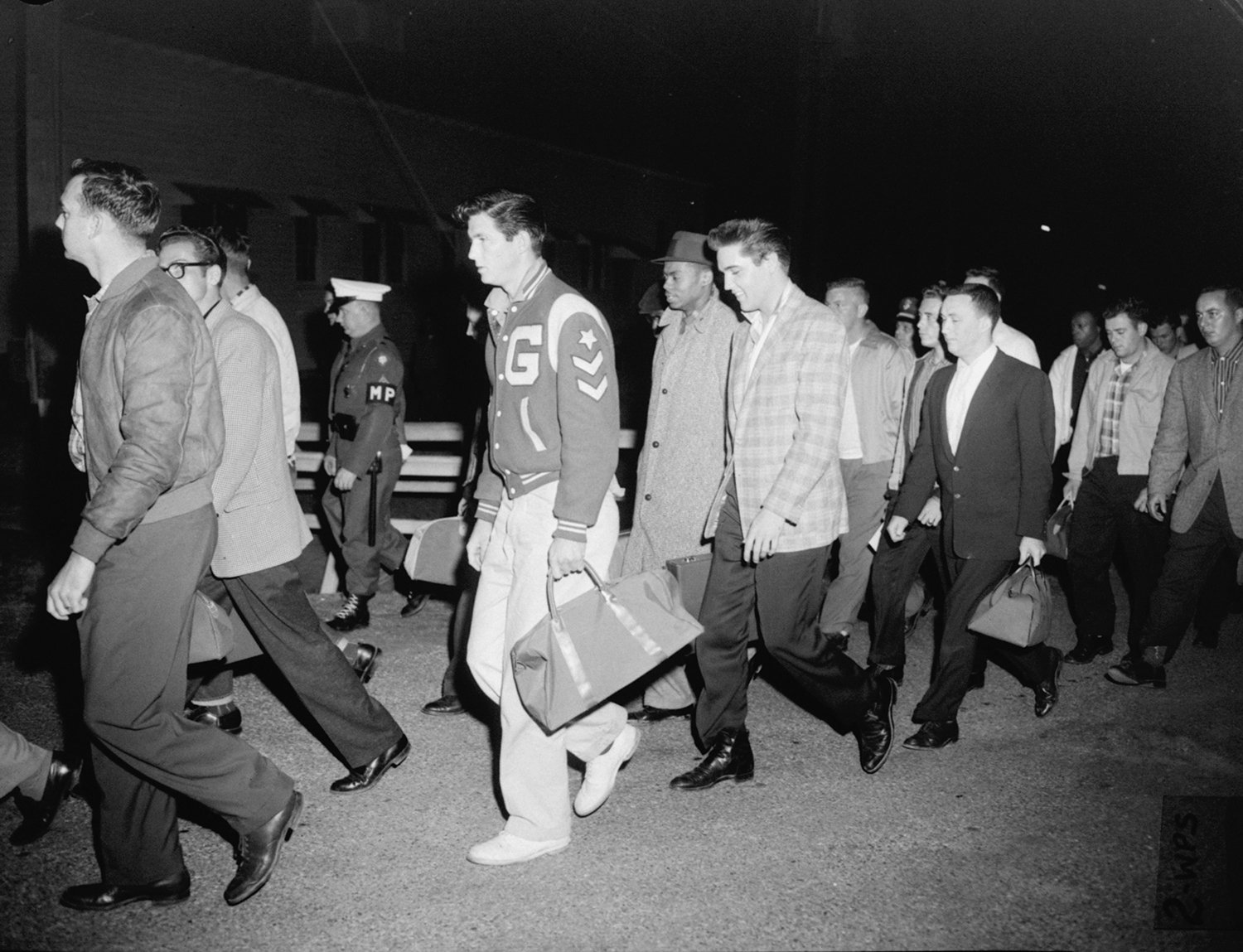  Singer Elvis Presley, in checkered sport coat, and other recruits are shown in their first Army maneuver, a walk from a bus to a supply building where they received their first G.I. issue bedding for the night. Elvis and 21 others arrived at Fort Ch