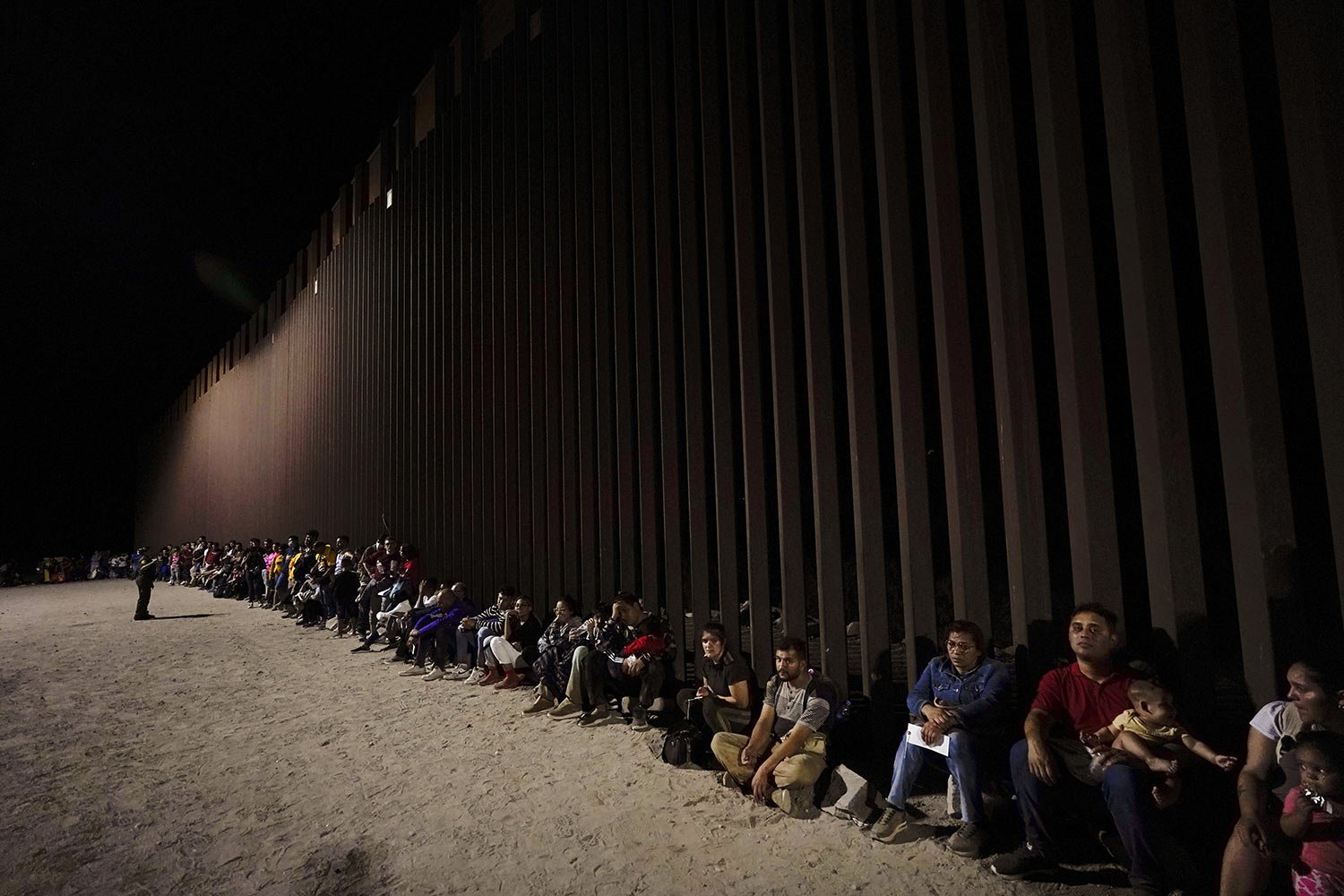  Migrants wait along a border wall after crossing from Mexico, near Yuma, Ariz., Tuesday, Aug. 23, 2022. (AP Photo/Gregory Bull) 