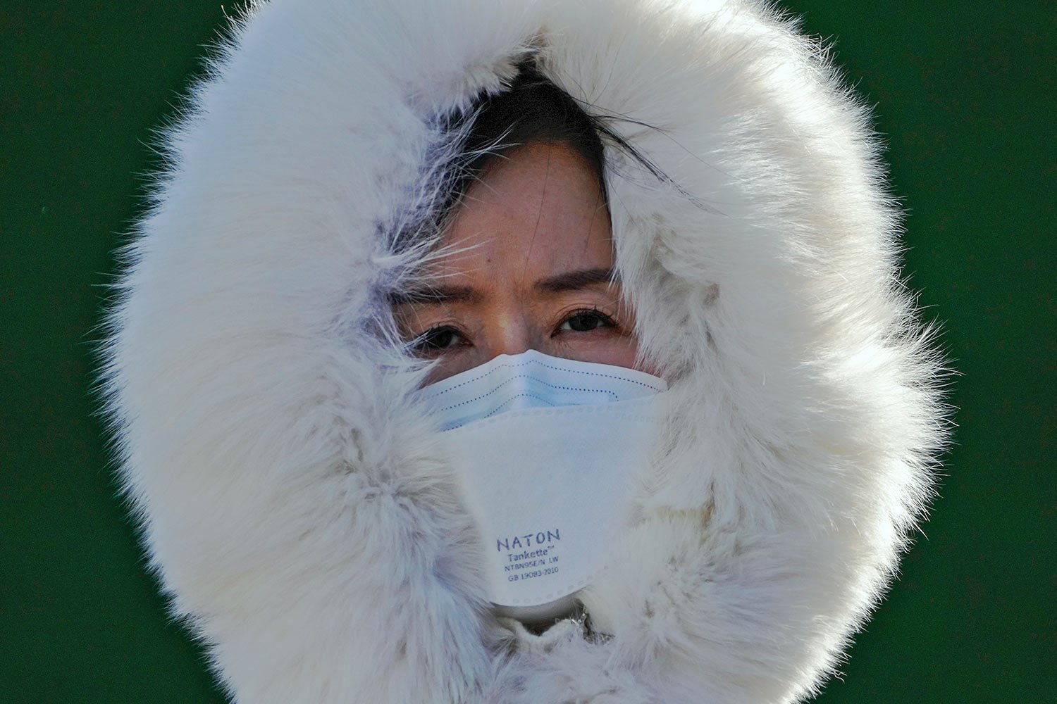  A woman wearing a face mask and covered with a fur hood walks on a street as the capital city is hit by cold wind in Beijing, Sunday, Dec. 11, 2022. (AP Photo/Andy Wong) 