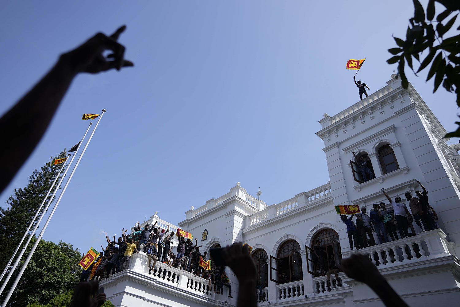  A protester waves the Sri Lanka flag from the roof of Prime Minister Ranil Wickremesinghe's office, demanding he resign after President Gotabaya Rajapaksa fled the country amid an economic crisis in Colombo, Sri Lanka, July 13, 2022. (AP Photo/Erang