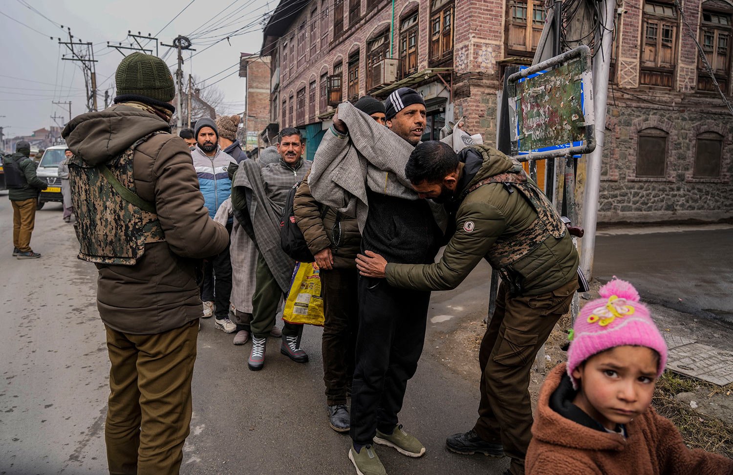  A child looks on as Indian policemen frisk Kashmiri pedestrians during a surprise security check in Srinagar, Indian controlled Kashmir, Monday, Jan. 9, 2023. (AP Photo/Mukhtar Khan) 