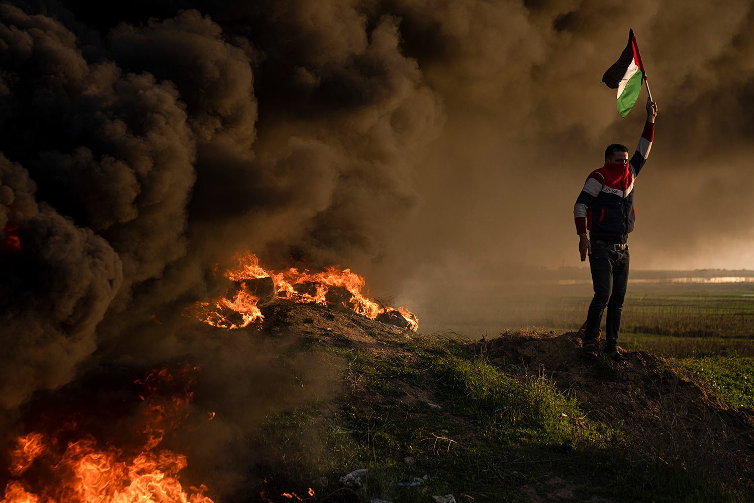  Palestinians burn tires and wave the national flag during a protest against Israeli military raid in the West Bank city of Jenin, along the border fence with Israel, in east of Gaza City, Thursday, Jan. 26, 2023. (AP Photo/Fatima Shbair) 