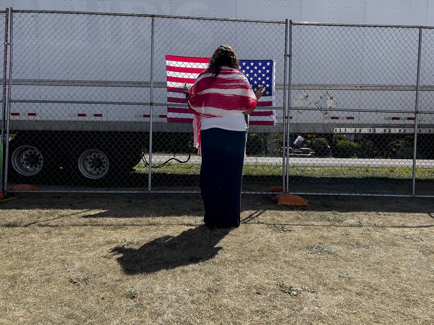  A woman prays facing a U.S. flag on the perimeter fence at the ReAwaken America Tour at Cornerstone Church in Batavia, N.Y., Aug. 13, 2022. (AP Photo/Carolyn Kaster) 