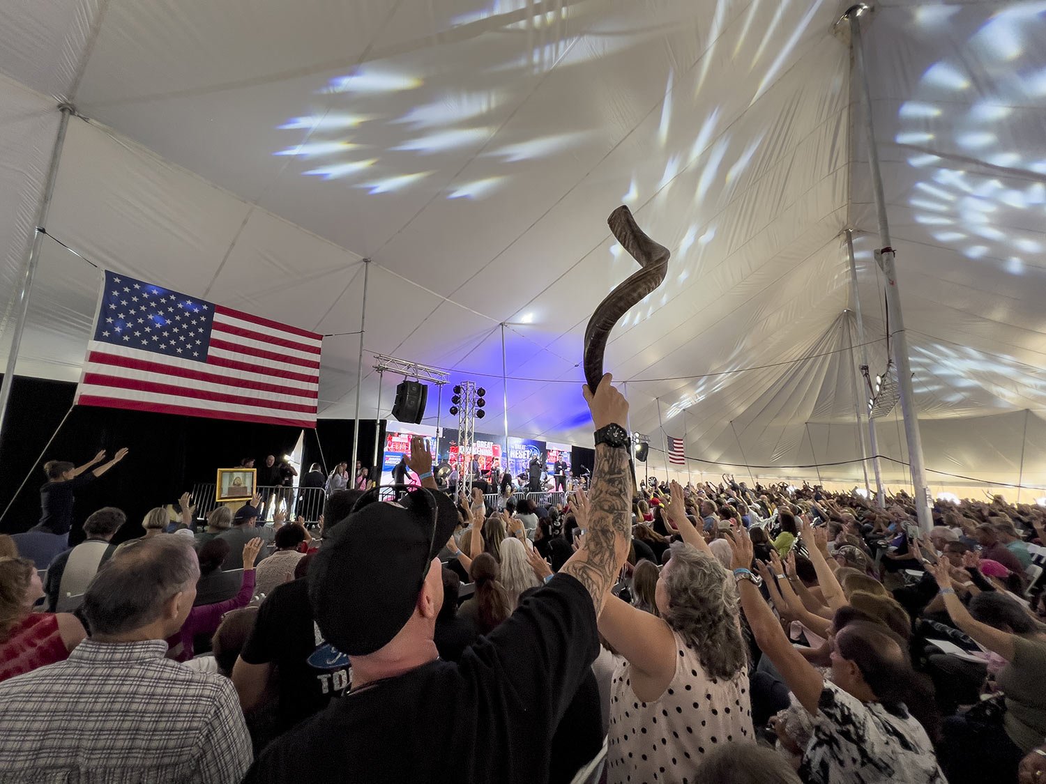  A man holds up a shofar as the audience prays inside a tent during the ReAwaken America Tour at Cornerstone Church in Batavia, N.Y., Aug. 12, 2022. The instrument, used in some Jewish worship services, has been adopted by the far right, and several 