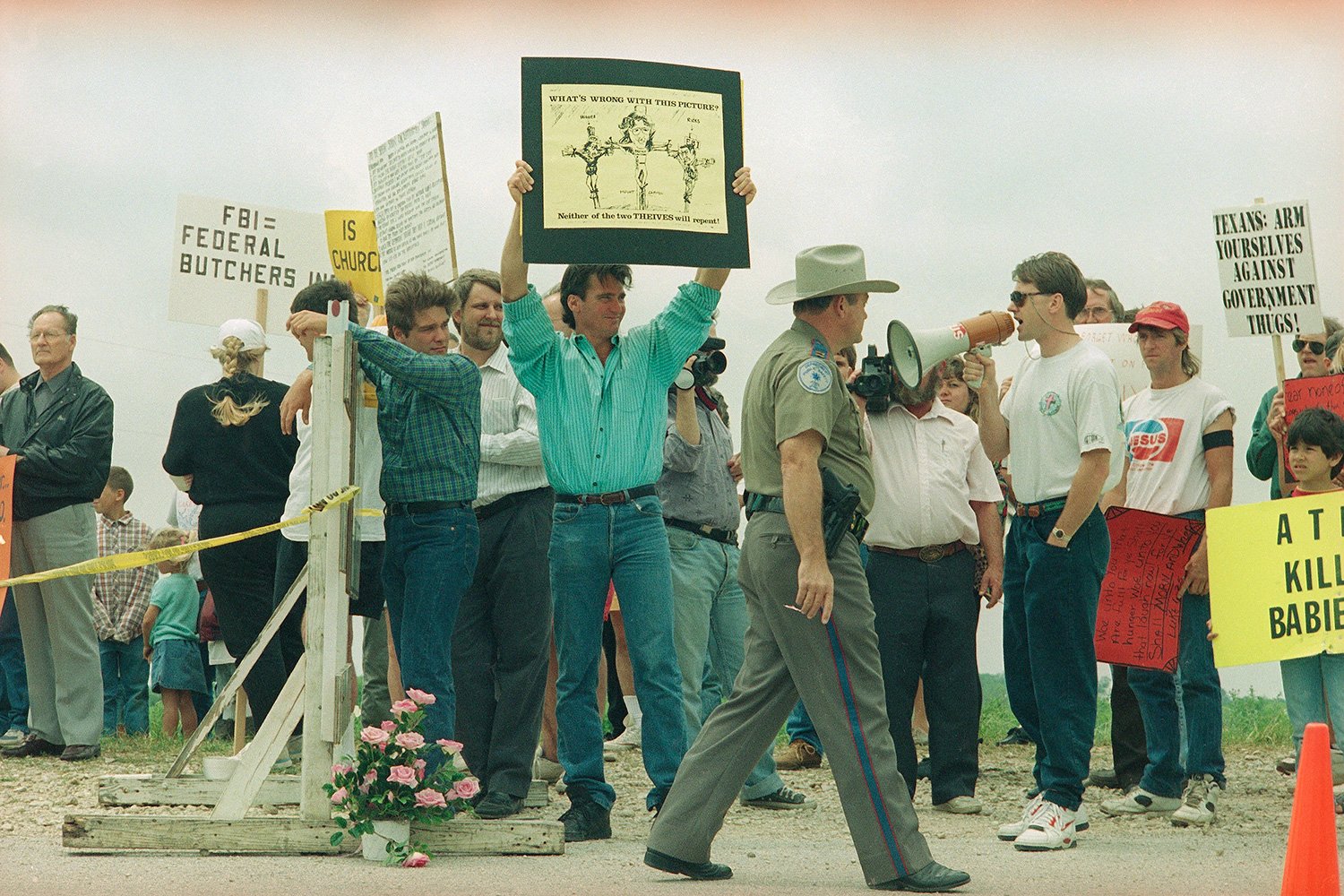  Demonstrators opposed to the FBI and ATF actions at the Branch Davidian compound, gather at a roadblock leading to the site near Waco, Texas, as a public safety officer walks past, April 24, 1993. (AP Photo/Susan Weems) 