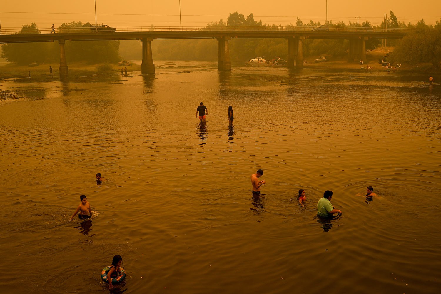  People wade in the river under a smoked-filled sky caused by wildfires in Renaico Chile, Saturday, Feb. 4, 2023. Wildfires in southern and central Chile triggered evacuations and the declaration of a state of emergency in some regions. (AP Photo/Mat