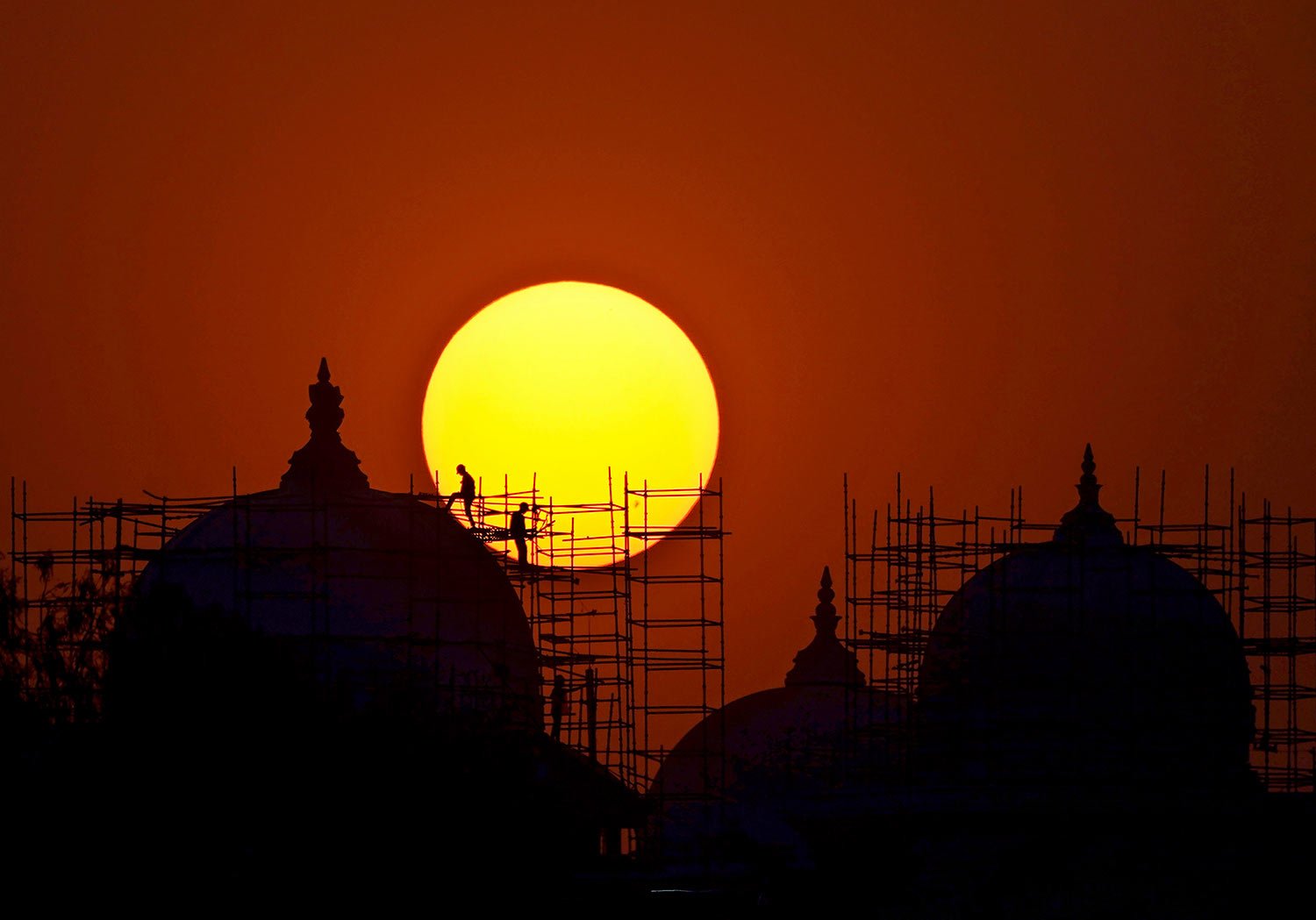  Workers are silhouetted against the setting sun at a construction site of a new Telangana State Secretariat building in Hyderabad, India, Tuesday, Feb. 28, 2023. (AP Photo/Mahesh Kumar A.) 