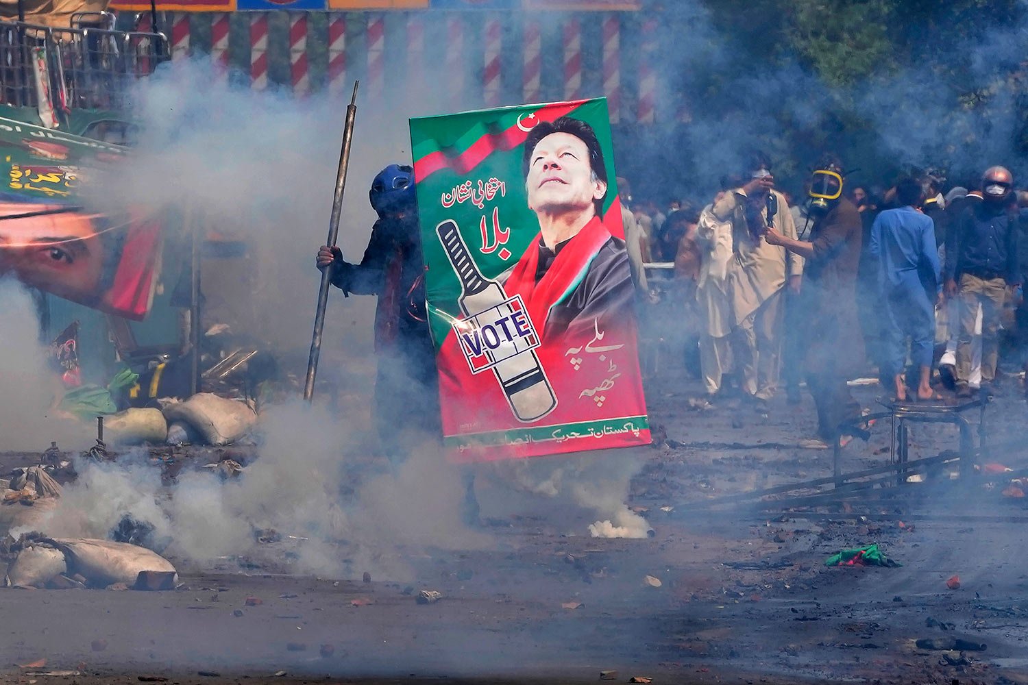  Supporters of former Prime Minister Imran Khan take cover after riot police officers fire tear gas to disperse them during clashes, in Lahore, Pakistan, Wednesday, March 15, 2023. (AP Photo/K.M. Chaudary) 