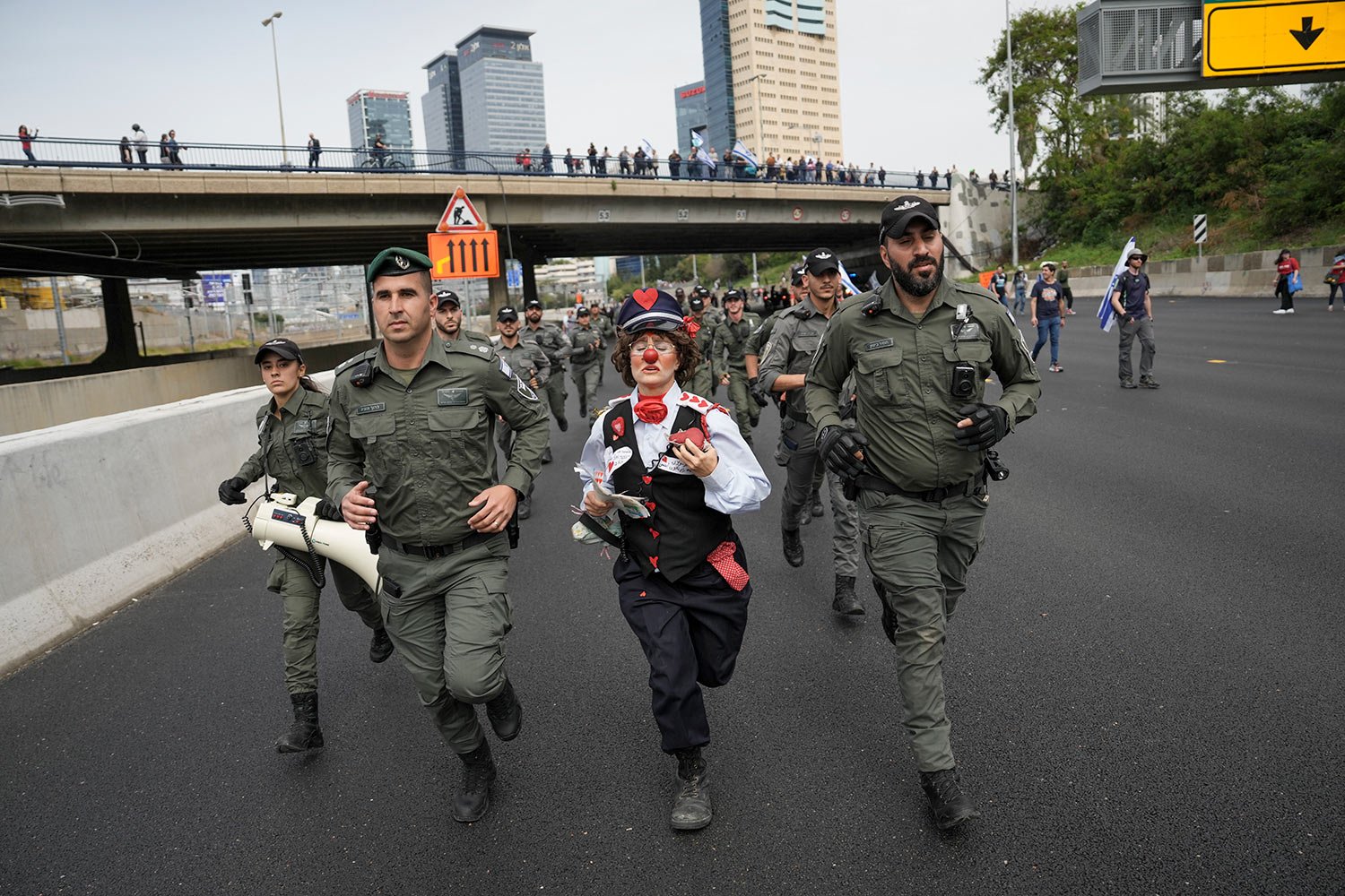  An Israeli activist dressed as a clown runs with border police as Israelis protest against plans by Prime Minister Benjamin Netanyahu's government to overhaul the judicial system block a free way in Tel Aviv, Israel, Thursday, March 23, 2023. (AP Ph