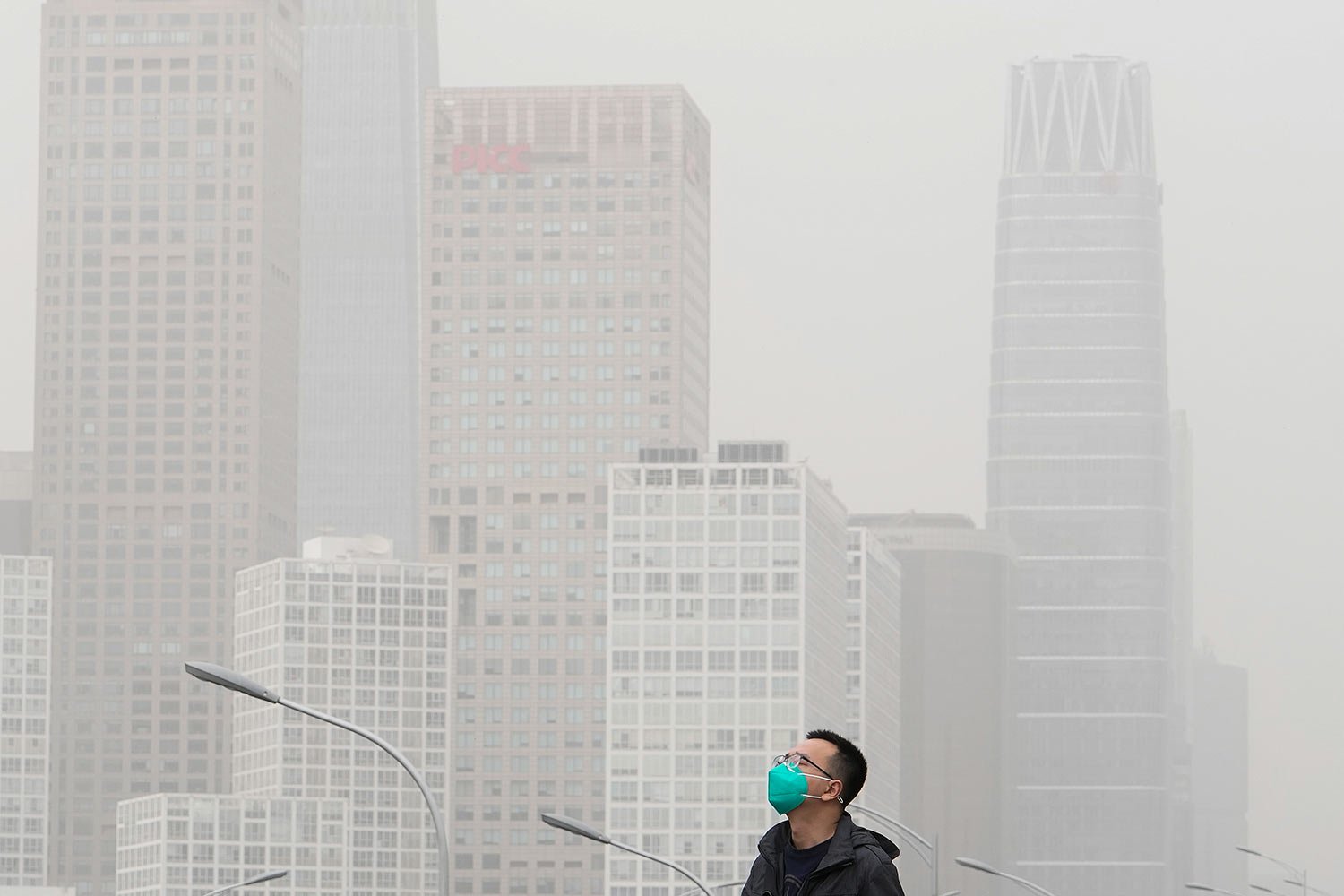  A man wearing a face mask walks on an overhead bridge against the office buildings in the central business district as dust and sand storm sweeps through Beijing, Thursday, April 13, 2023. (AP Photo/Andy Wong) 