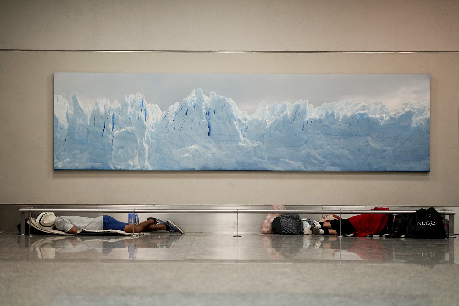  Homeless men sleep at the Jorge Newbery international airport under a photo of the Perito Moreno Glacier, in Buenos Aires, Argentina, April 6, 2023. More than 100 homeless people sleep nightly at the airport. (AP Photo/Natacha Pisarenko) 