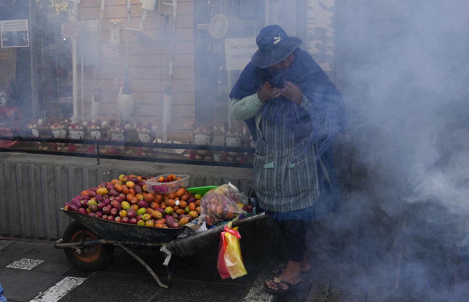  A fruit vendor covers her face amid tear gas fired by police during clashes with protesting teachers near the government palace in La Paz, Bolivia, April 12, 2023. Teachers demand more pay and protest the new public school curriculum. (AP Photo/Juan