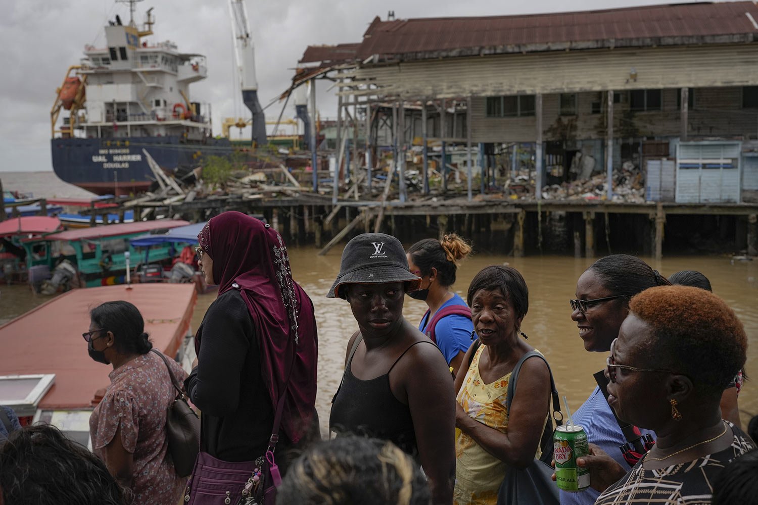  People wait at the Stabroek Market to ferry across the Demerara River, as a container ship is anchored behind them in Georgetown, Guyana, April 12, 2023. Guayana is poised to become the world’s fourth-largest offshore oil producer, placing it ahead 
