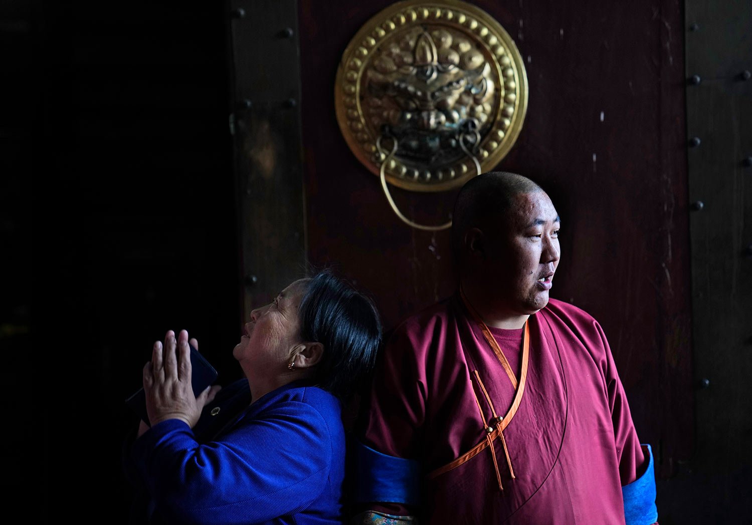  A Mongolian woman prays as a monk stands at the entrance of the Gandan Buddhist monastery on the first day of summer, in Ulaanbaatar, the capital of Mongolia, Monday, May 22, 2023. (AP Photo/Manish Swarup) 
