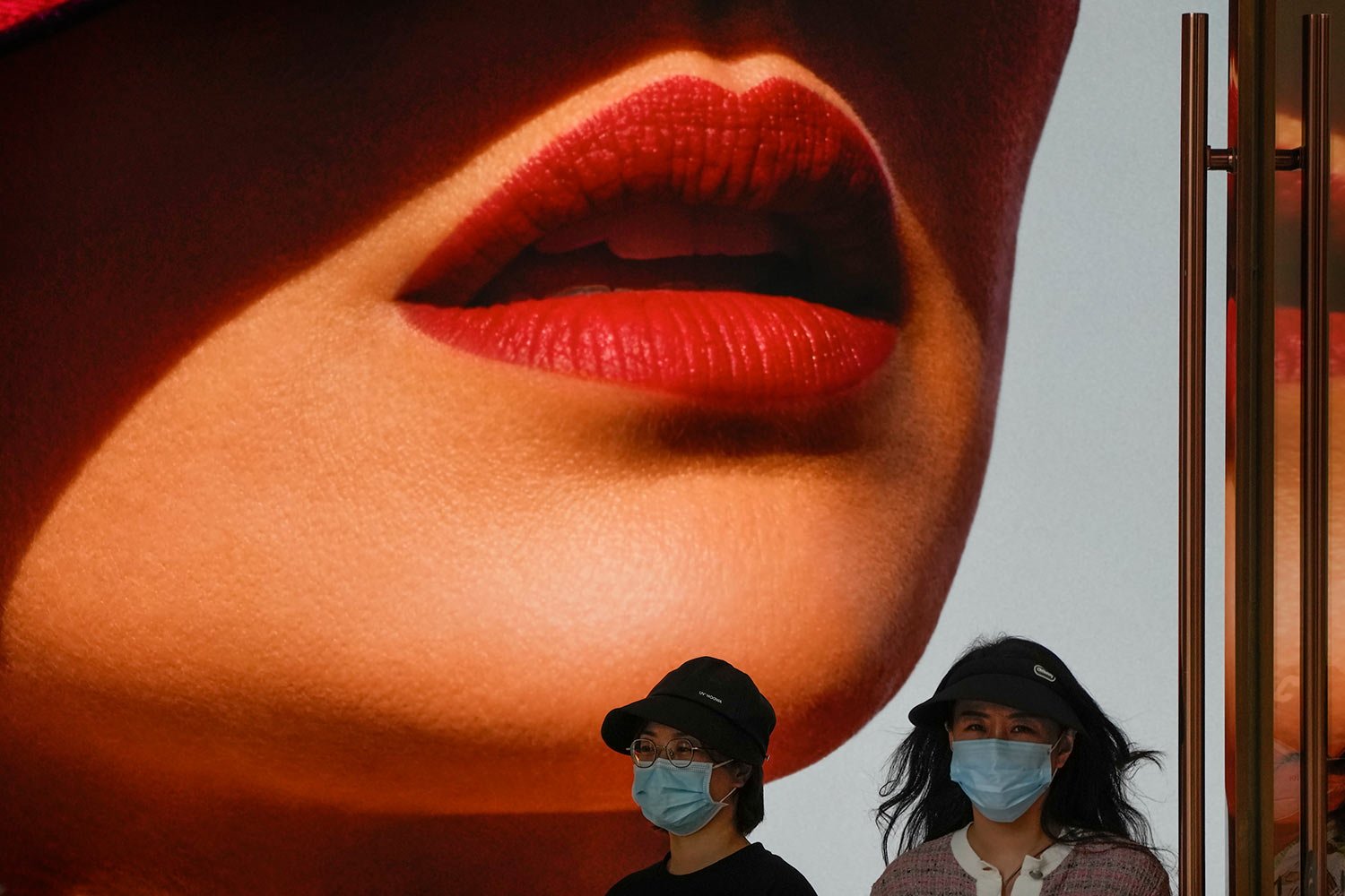  Women wearing face masks walk by a lipstick advertisement on display at a shopping mall in Beijing, Monday, May 15, 2023. (AP Photo/Andy Wong) 