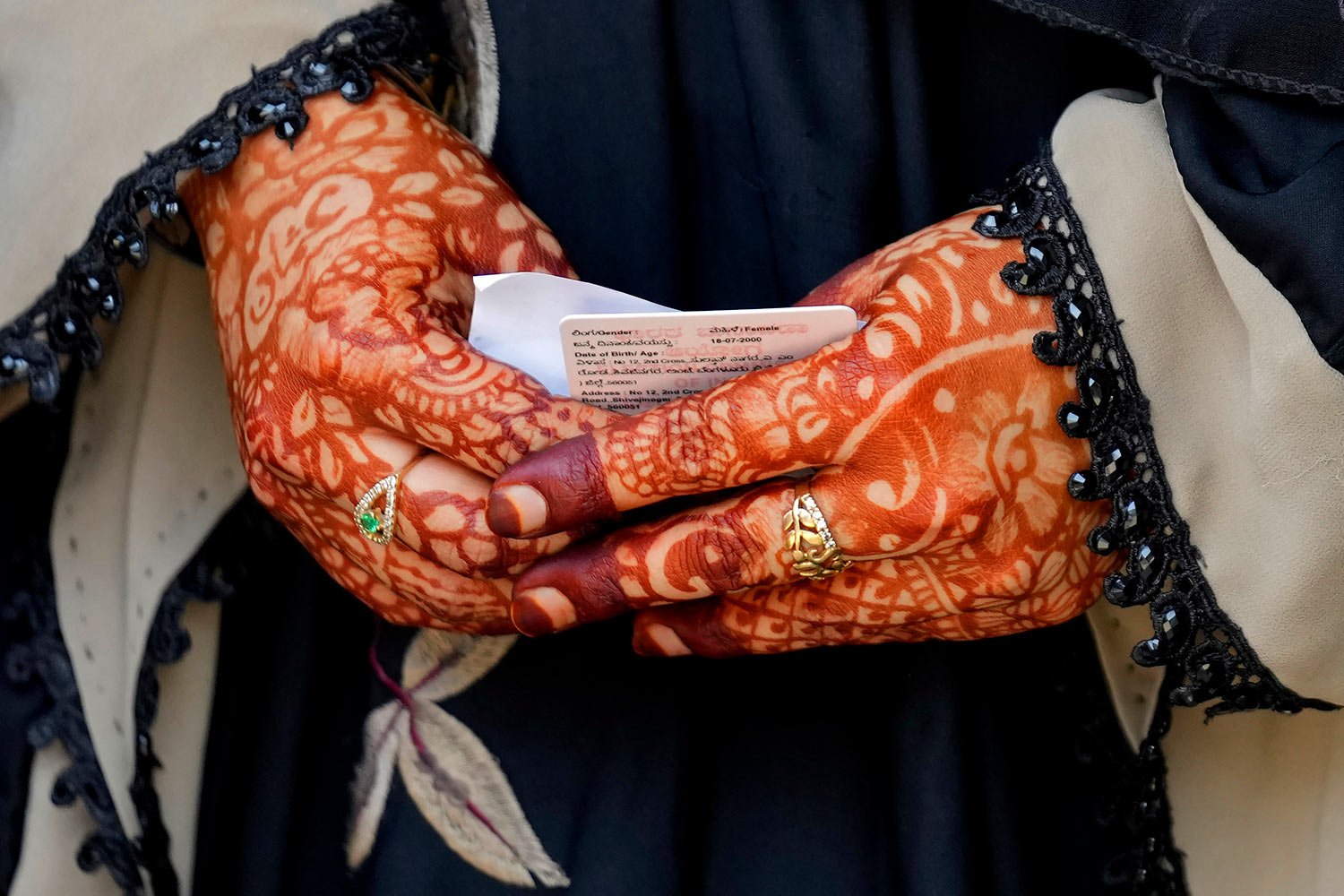  A woman with her hands decorated with henna holds her voter identity card as she waits to cast her vote at a polling station in Bengaluru, India, Wednesday, May 10, 2023. (AP Photo/Aijaz Rahi) 