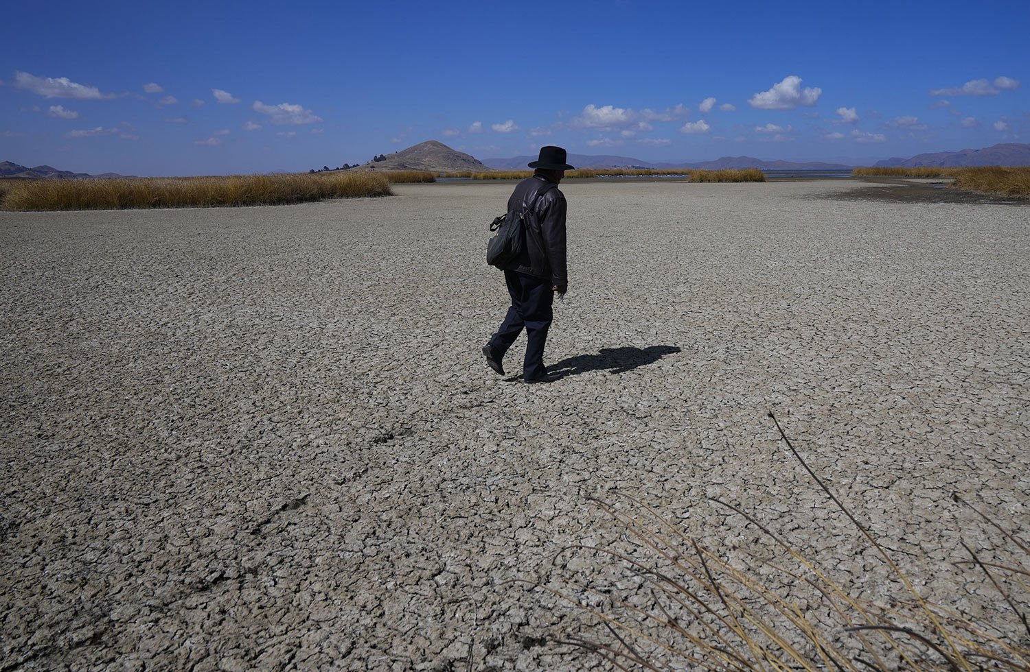 An Aymara man walks on the dry cracked bed of Lake Titicaca where they’re used to water, in Huarina, Bolivia, Thursday, July 27, 2023.  The highest navigable lake in the world has receded to what Bolivian authorities say are critically low levels du