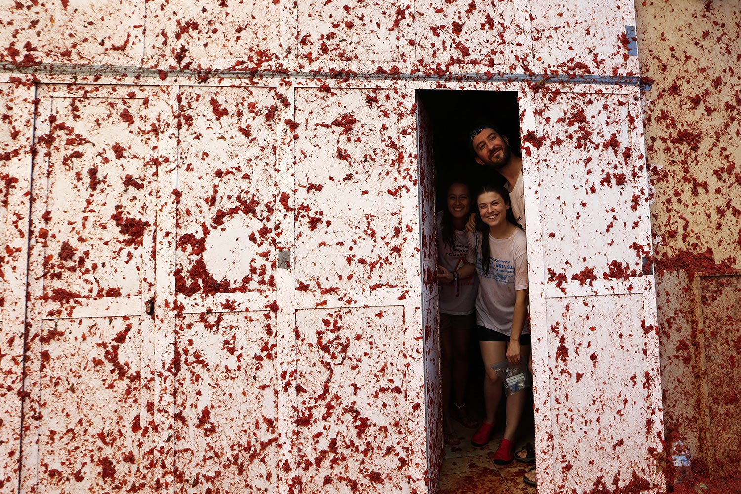  People peek out from inside a home whose facade is slathered with tomato pulp during the annual “Tomatina” festival, in Bunol, Spain, Wednesday, Aug. 30, 2023. (AP Photo/Alberto Saiz) 