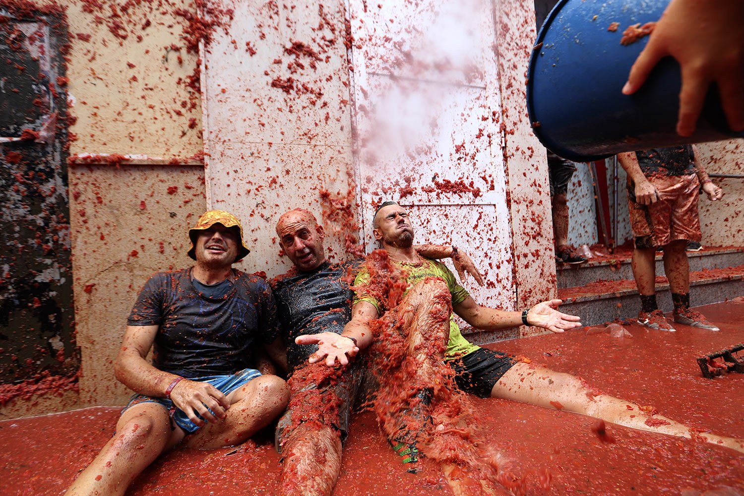  People covered with bits of tomato sit in a pool of red pulp during the annual “Tomatina” street fight, in Bunol, Spain, Wednesday, Aug. 30, 2023. (AP Photo/Alberto Saiz) 