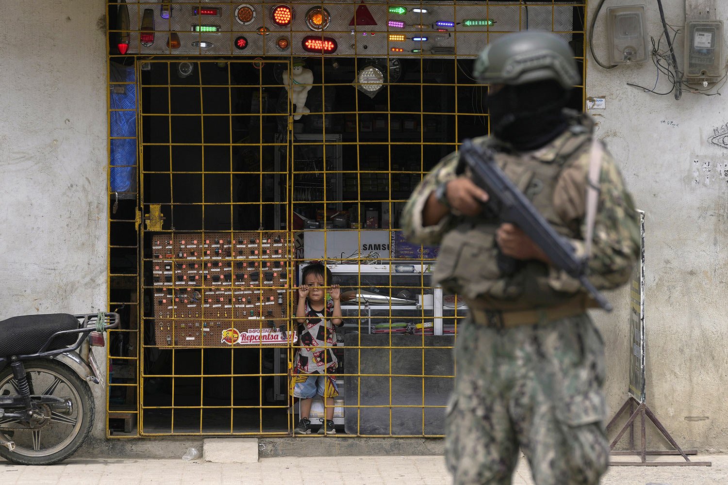  A toddler watches from behind a storefront gate where a soldier stands guard at a security check point in Duran, Ecuador, Aug. 14, 2023, during a state of emergency triggered by the assignation of a presidential candidate. (AP Photo/Martin Mejia) 