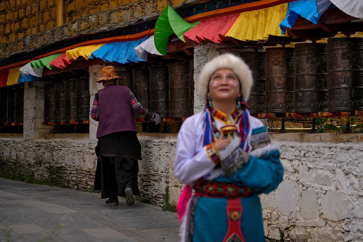 A woman wearing a Tibetan costume looks up as a Tibetan woman turns the prayer wheels surrounding the Renkang House, the birth place of the seven Dalai Lama, at the thousand-household Tibetan village, one of the tourism spot in Litang county, Ganzi 
