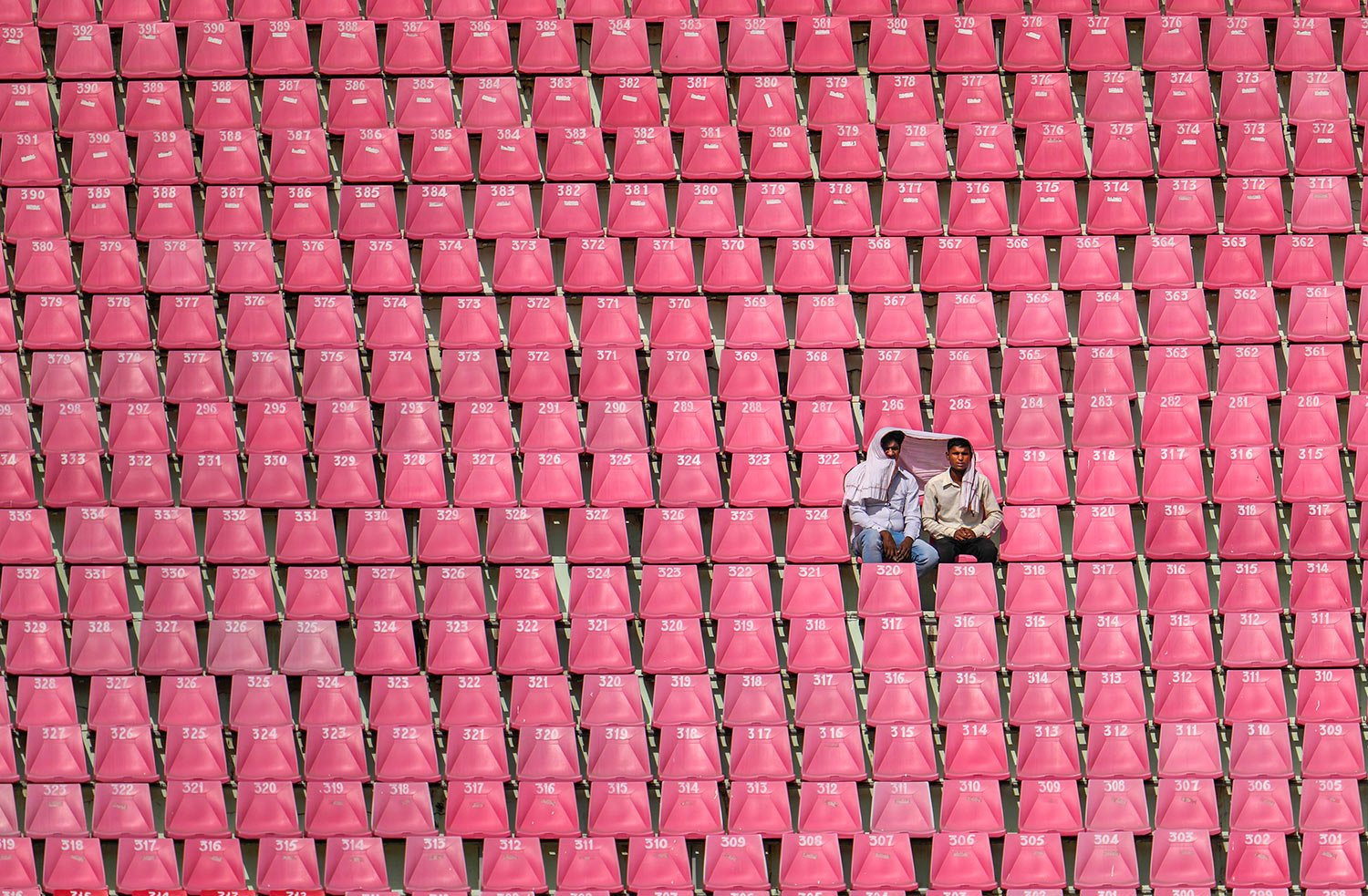  Two men share a piece of cloth to protect from the sun as they watch from a deserted gallery the ICC Cricket World Cup match between Australia and South Africa in Lucknow, India, Thursday, Oct. 12, 2023. (AP Photo/Altaf Qadri ) 