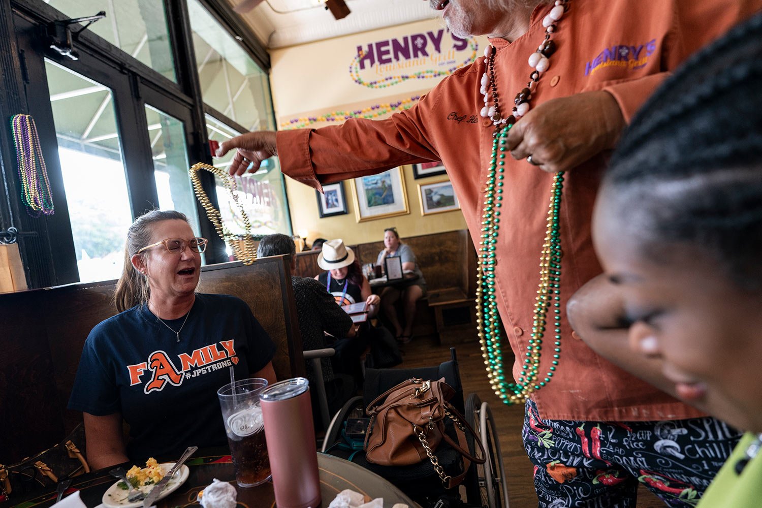  Henry Chandler tosses beads over the head of Janet Paulson, left, as she dines for lunch at his restaurant, Henry’s Louisiana Grill with with Tanesha McAuley, right, of the Cobb County Family Justice Center, in Acworth, Ga., Tuesday, Aug. 8, 2023. (