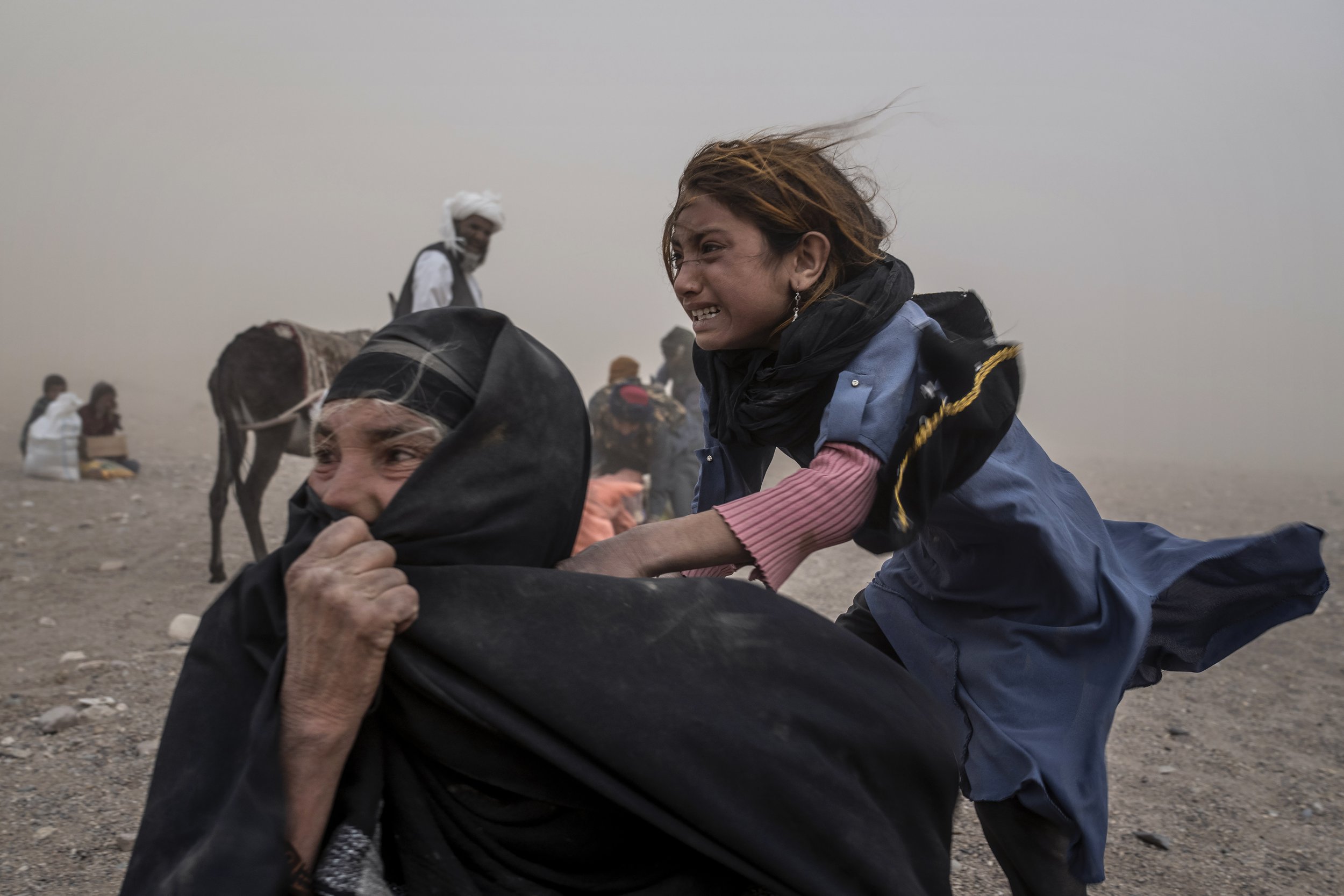  An Afghan girl and woman, frightened and crying, brace themselves against the wind in a fierce sandstorm as they try to receive aid following an earthquake that killed more than 2,000 people and flattened whole villages in the Zenda Jan district of 