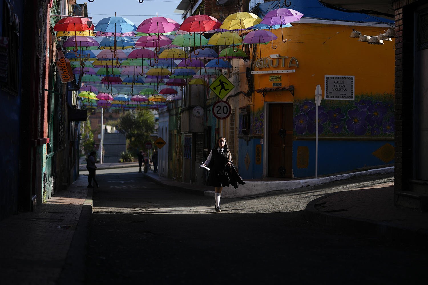  A student walks past a canopy of umbrellas adorning the Calle de las Violetas in La Candelaria, a downtown neighborhood of Bogota, Colombia, Nov. 22, 2023. (AP Photo/Fernando Vergara) 