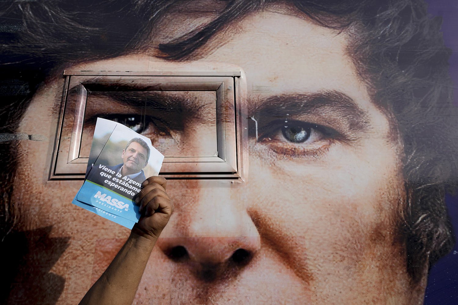 A supporter of the ruling party presidential candidate, holds up flyers promoting Sergio Massa in front of a campaign bus emblazoned with an image of opponent Javier Milei, in Ezeiza, Buenos Aires province, Nov. 15, 2023. (AP Photo/Natacha Pisarenko