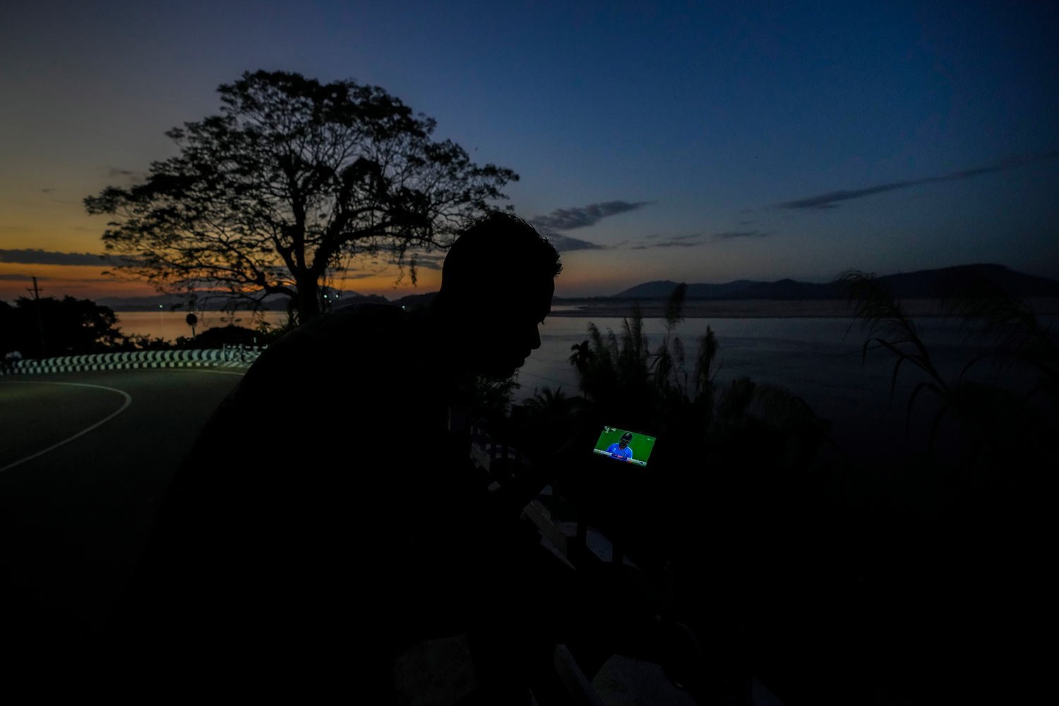  A man watches the ICC Men's Cricket World Cup final match between Australia and India on his mobile phone along the river Brahmaputra in Guwahati, India, Sunday, Nov. 19, 2023. (AP Photo/Anupam Nath) 