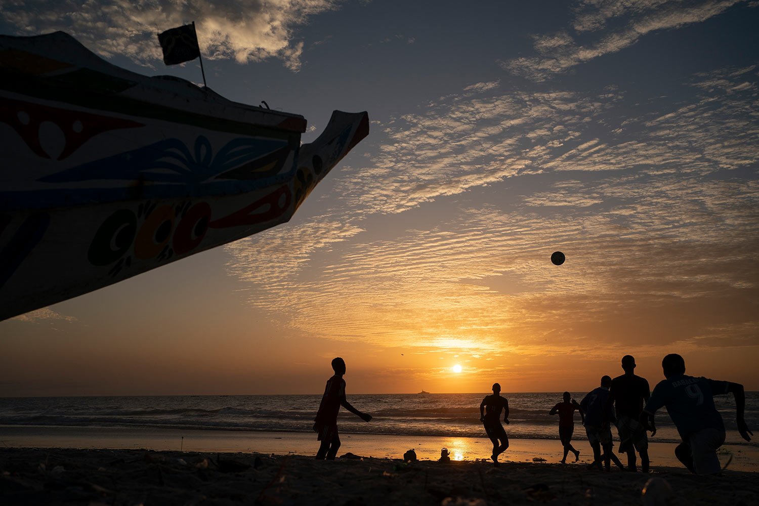  Silhouetted against the setting sun, youths play soccer next to a pirogue docked on the beach in Saint Louis, Senegal, Thursday, Jan. 19, 2023. (AP Photo/Leo Correa) 