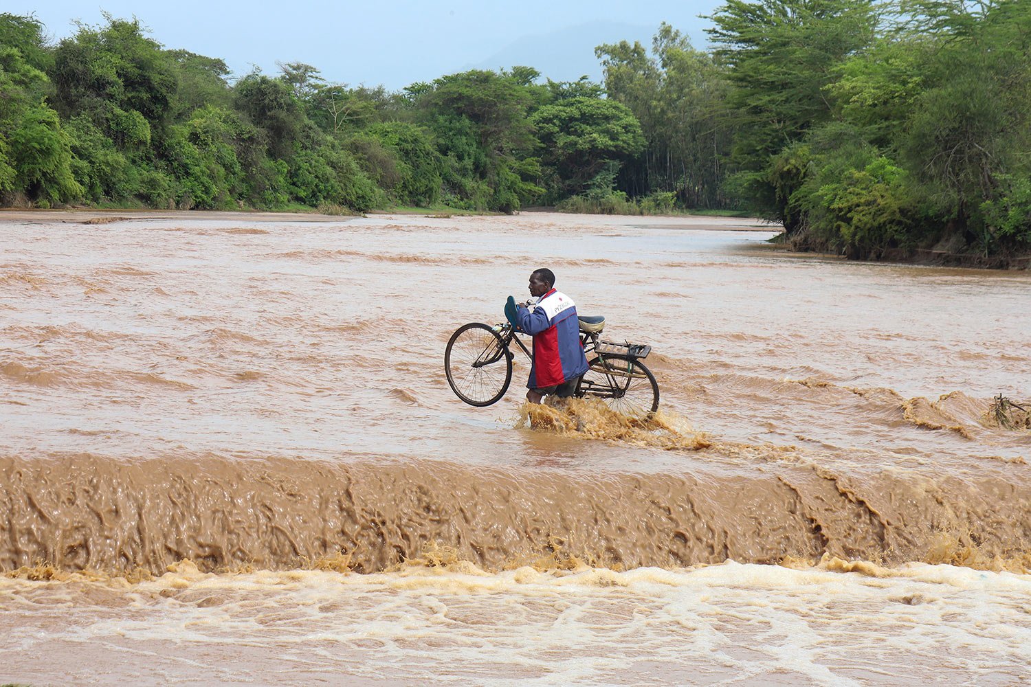  A man carrying his bicycle crosses through a flooded Muuoni River, where 8 people are said to have drowned overnight while crossing the river at Mukaa area, Makueni county, Kenya's Eastern region, Friday, Nov. 24, 2023. (AP Photo) 