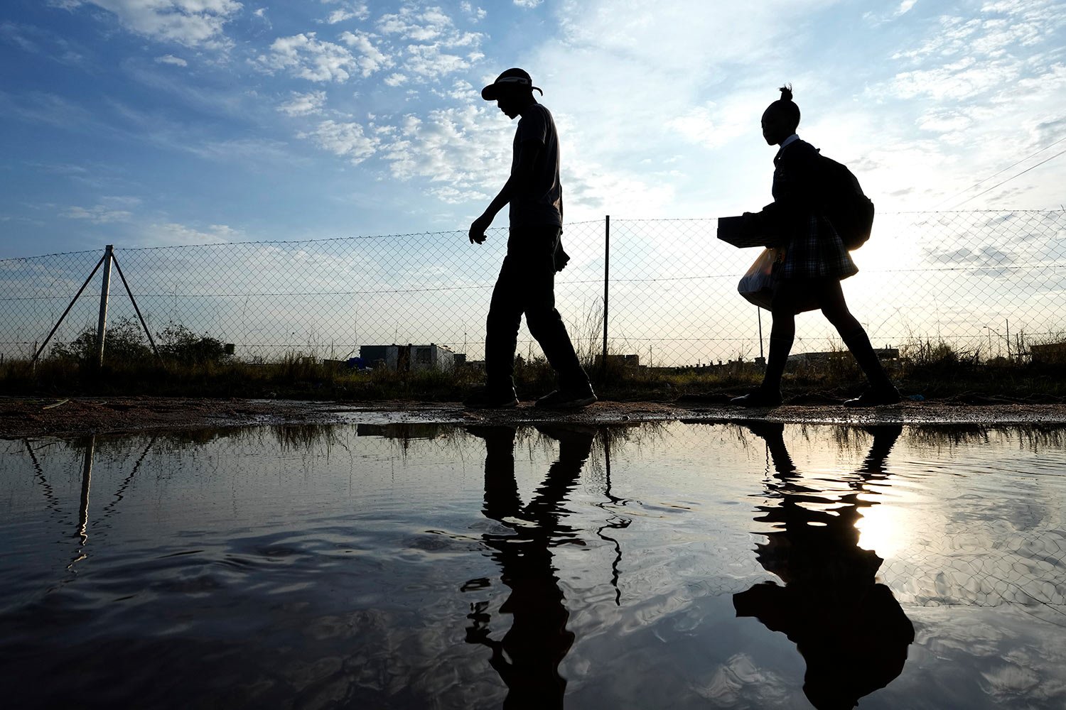  A man and woman walk over puddled water along a street from an overflowing reservoir in Hamanskraal, Pretoria, South Africa, Friday, May 26, 2023. (AP Photo/Themba Hadebe) 