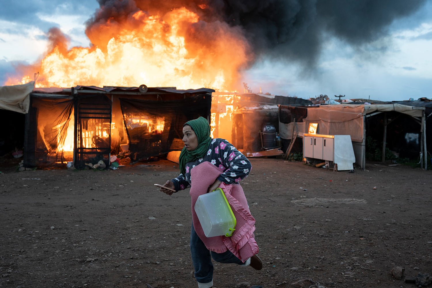  A woman runs past burning shacks during a fire before an eviction by police officers in Almeria, Spain, Monday, Jan. 30, 2023.  (AP Photo/Santi Donaire) 