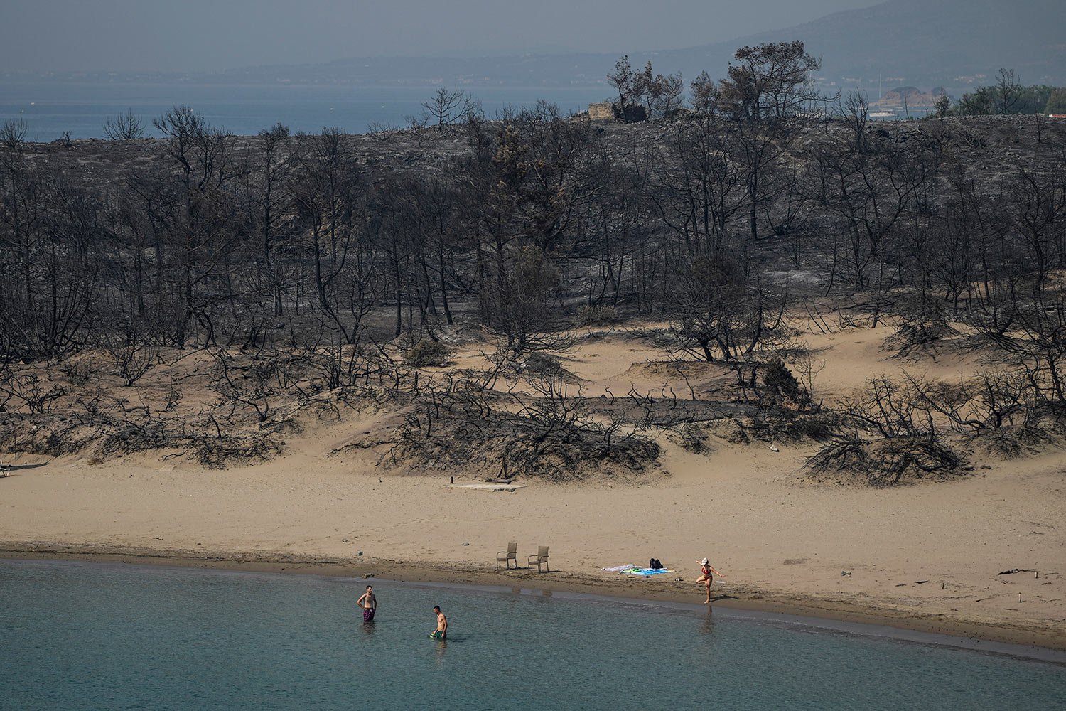  People gather on a beach in front of burnt forest near Gennadi village, on the Aegean Sea island of Rhodes, southeastern Greece, on Thursday, July 27, 2023. (AP Photo/Petros Giannakouris) 