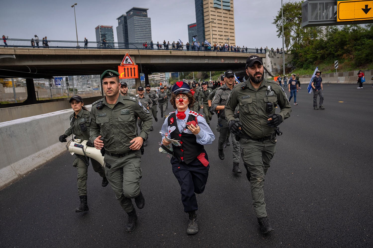  An Israeli activist dressed as a clown runs with border police as Israelis protest against plans by Prime Minister Benjamin Netanyahu's government to overhaul the judicial system block a free way in Tel Aviv, Israel, Thursday, March 23, 2023. (AP Ph