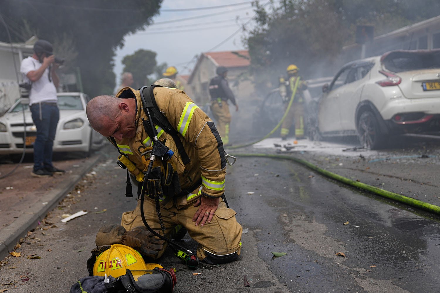  An Israeli firefighter kneels to compose himself after he and his colleagues extinguished cars set on fire by a rocket fired from the Gaza Strip in Ashkelon, Israel, Monday, Oct. 9, 2023. (AP Photo/Ohad Zwigenberg) 