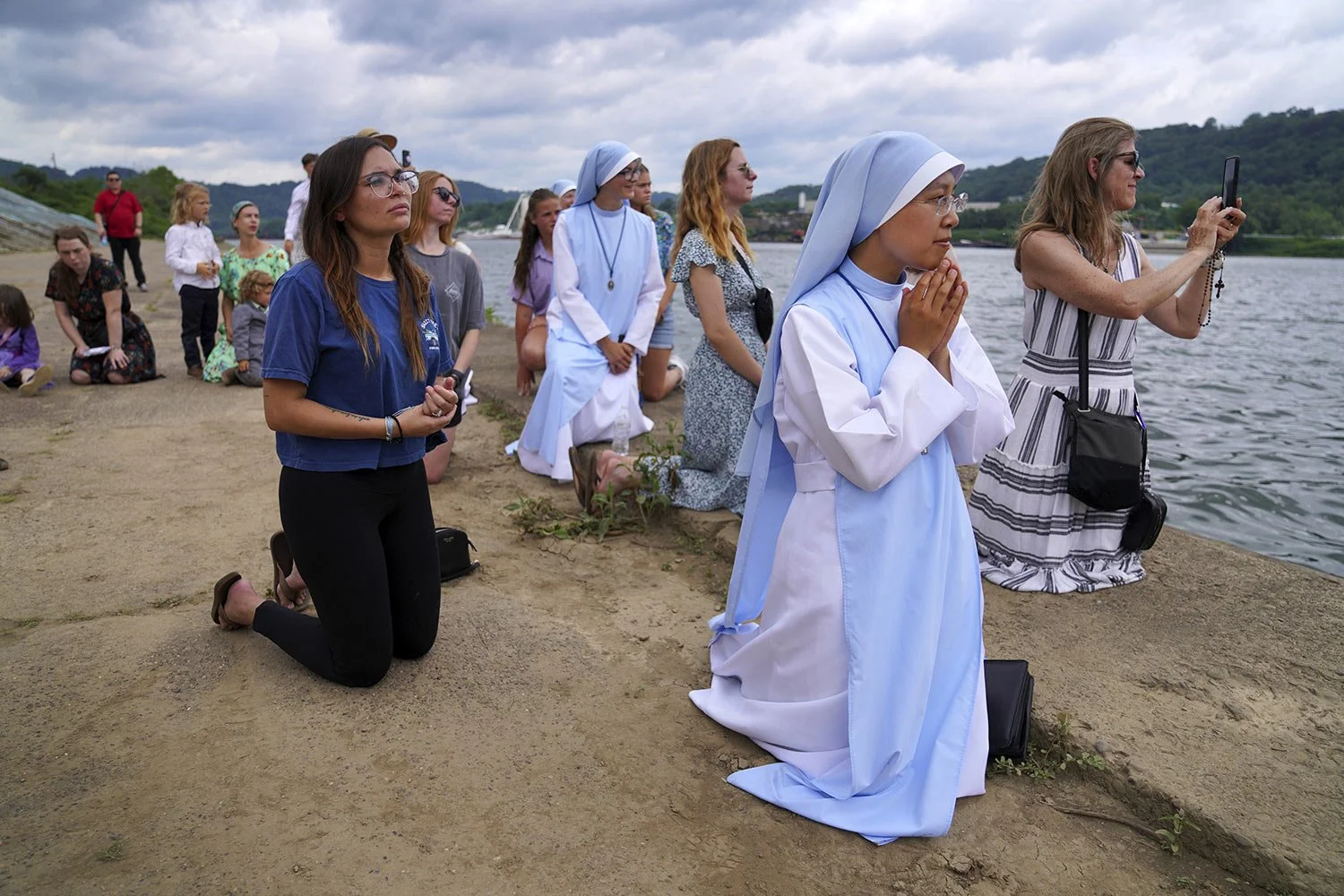  Sister Mary Fatima Pham, second from right, kneels with her fellow Catholics as they watch the Eucharist brought on board a boat on the Ohio River at the Steubenville Marina in Steubenville, Ohio, Sunday, June 23, 2024. The National Eucharistic Pilg