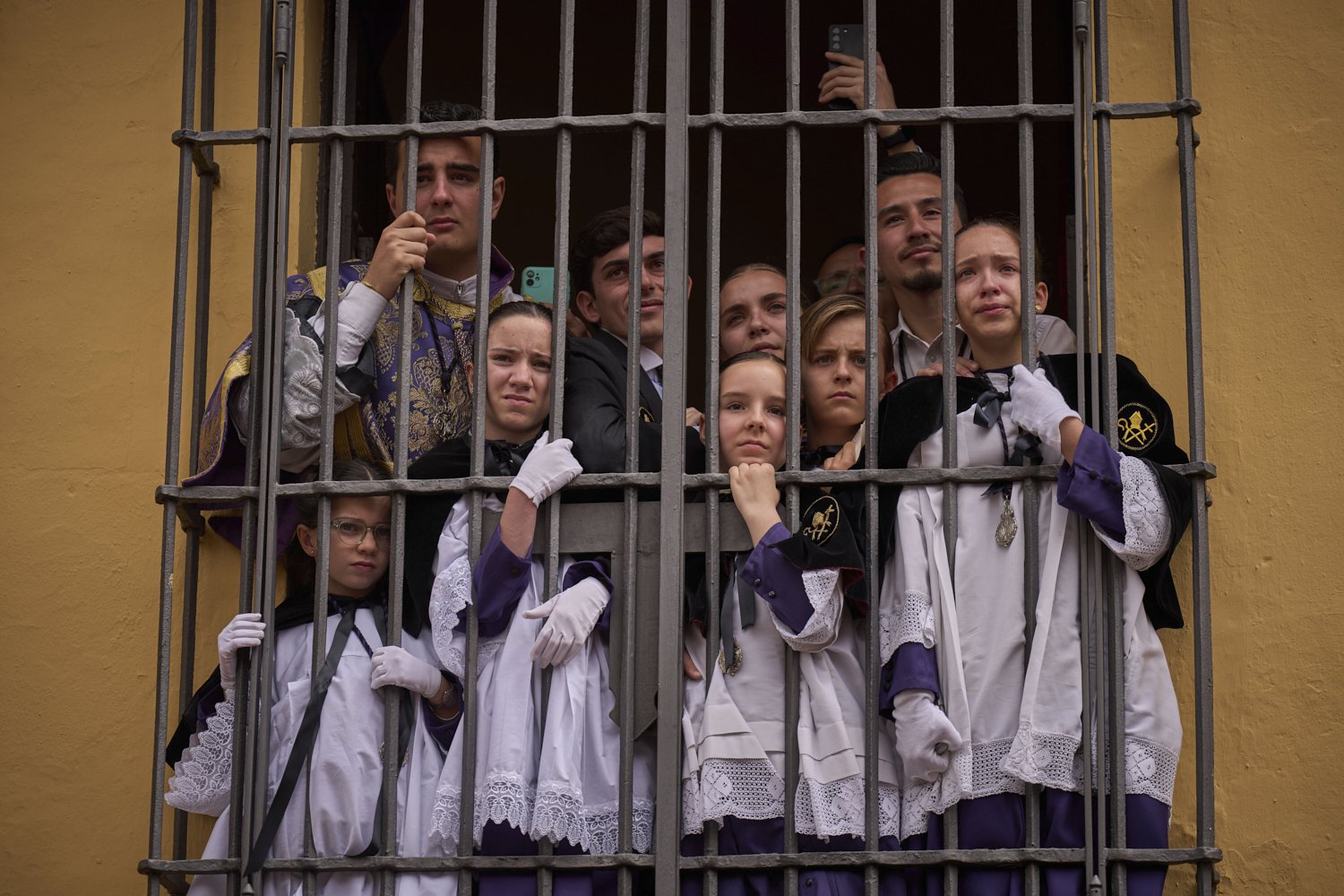 Altar servers crowd a window to watch the passing of the Christ of the San Bernardo brotherhood during Holy Week in Seville, Spain, Wednesday April 16, 2025. (AP Photo/Emilio Morenatti)