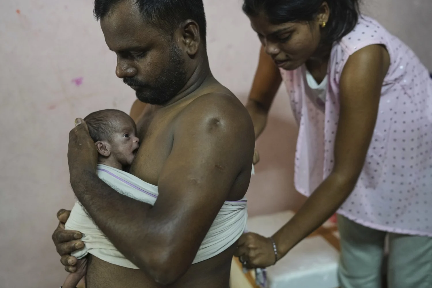 Antima Kumari helps Sikandar Chaudhary, her brother-in-law, with the Kangaroo Mother Care (KMC), a method of holding a baby skin-to-skin on the caregiver's chest, to promote bonding and well-being for her newborn niece at their house in Gurugram, a