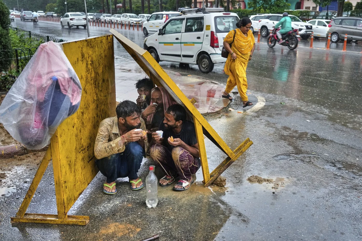 Laborers drink tea, sitting under tin shade panels to shelter themselves from the rain during roadwork, in New Delhi, India, Monday, Sept. 1, 2025. (AP Photo/Manish Swarup)