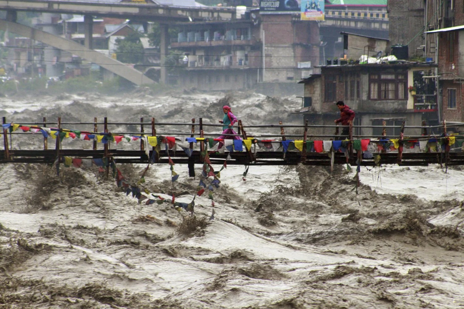 Residents run across a bridge over the flooded Beas River following incessant rains in Kullu, India, Aug. 26, 2025. (AP Photo/Aqil Khan)