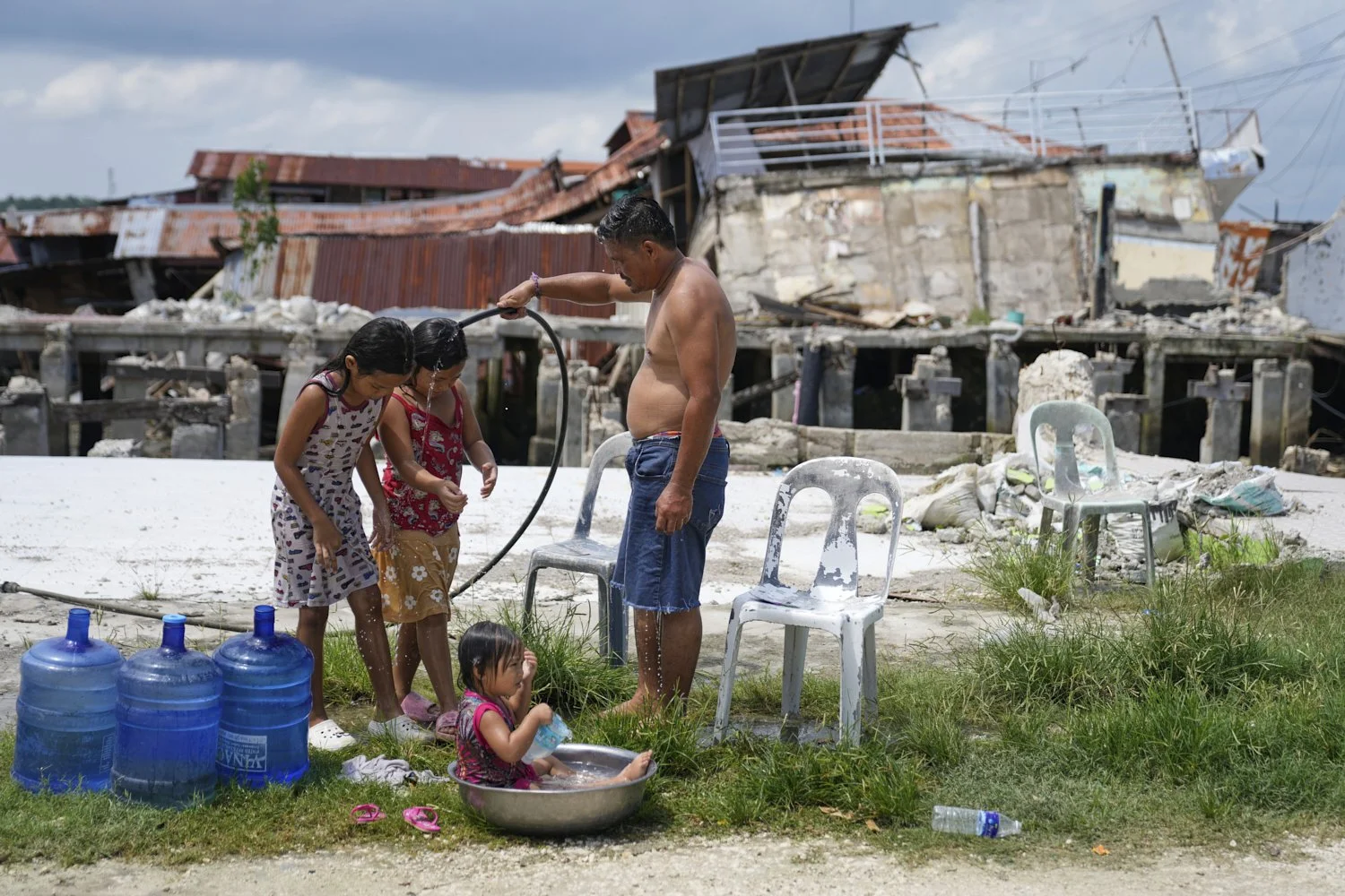  A man takes a bath with his daughters beside damaged structures due to a recent strong earthquake in Bogo, Cebu Province, Central Philippines, Oct. 3, 2025. (AP Photo/Aaron Favila) 